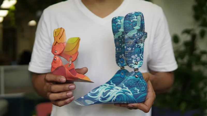 A person holding two colorful 3D-printed ankle-foot orthoses with printed graphic patterns