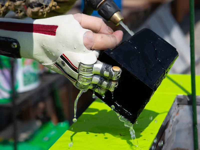 A Point Designs partial hand prosthesis gripping a black box under running water