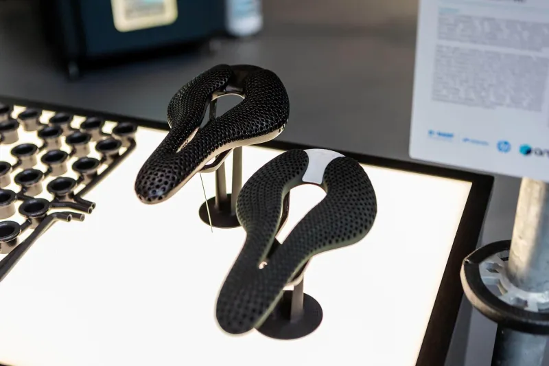 Two black 3D-printed lattice bicycle saddles on a display stand