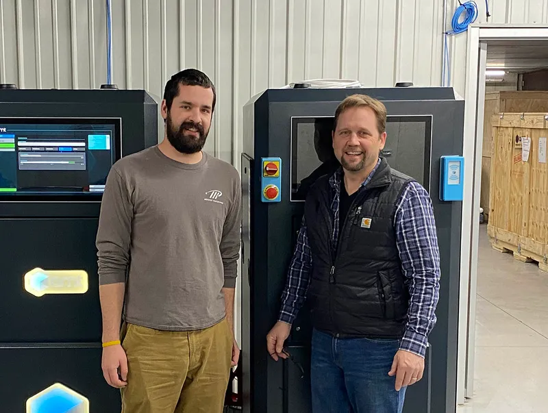 Two members of the Prototek team standing beside PostPro SF systems