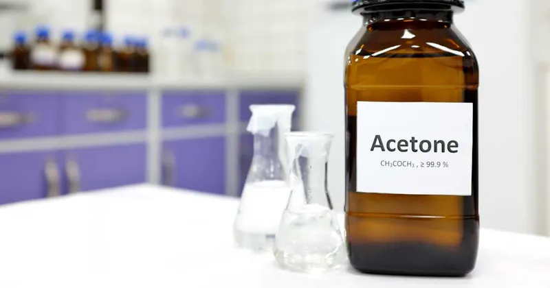 A brown laboratory bottle labeled Acetone next to glass flasks