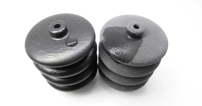 Two black 3D-printed bellows after a water test: the vapor-smoothed one stays glossy, the as-printed one shows wet patches