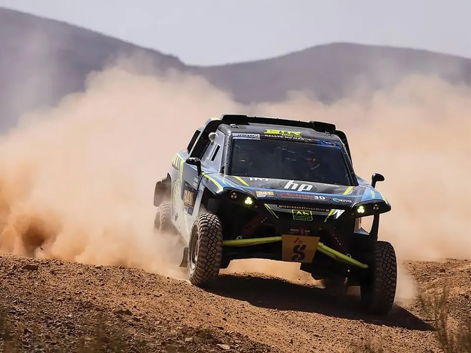 ABConcept rally car at speed on a desert stage, throwing up a plume of dust